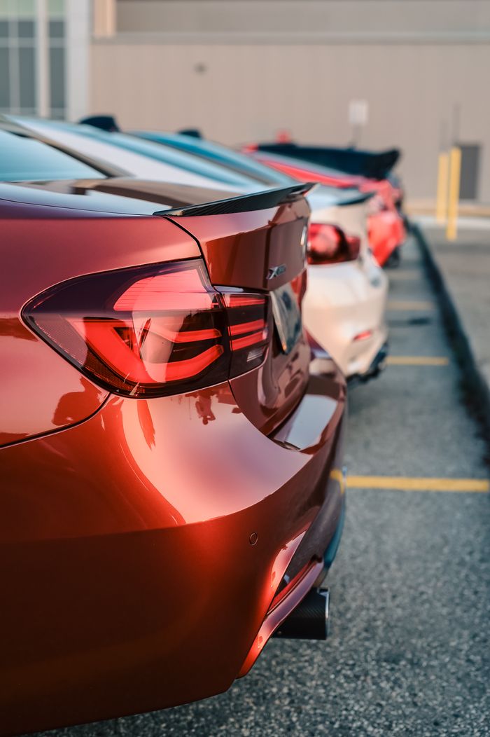 Close-up of parked cars highlighting the sleek design and tail lights, viewed from the back in a parking lot.