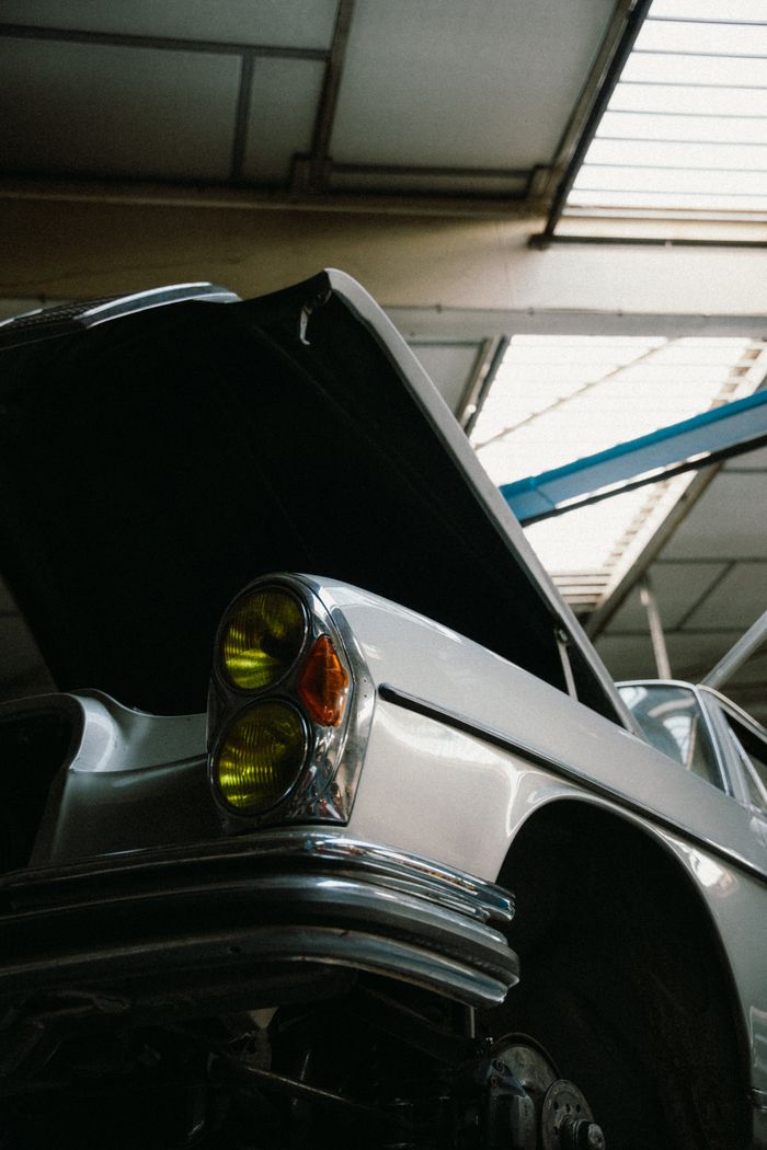 Vintage car with open hood in a garage, showcasing retro design and detailed craftsmanship.