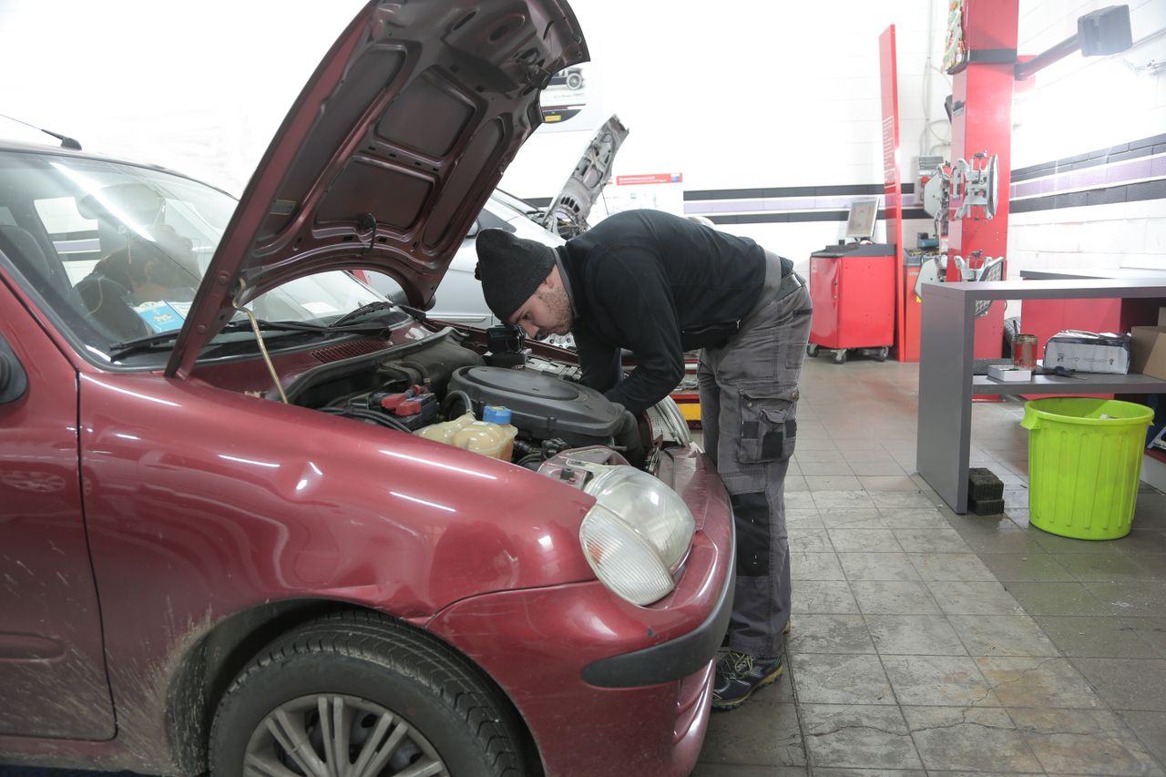 Mechanic performs engine inspection on a red car indoors, in a garage workshop.